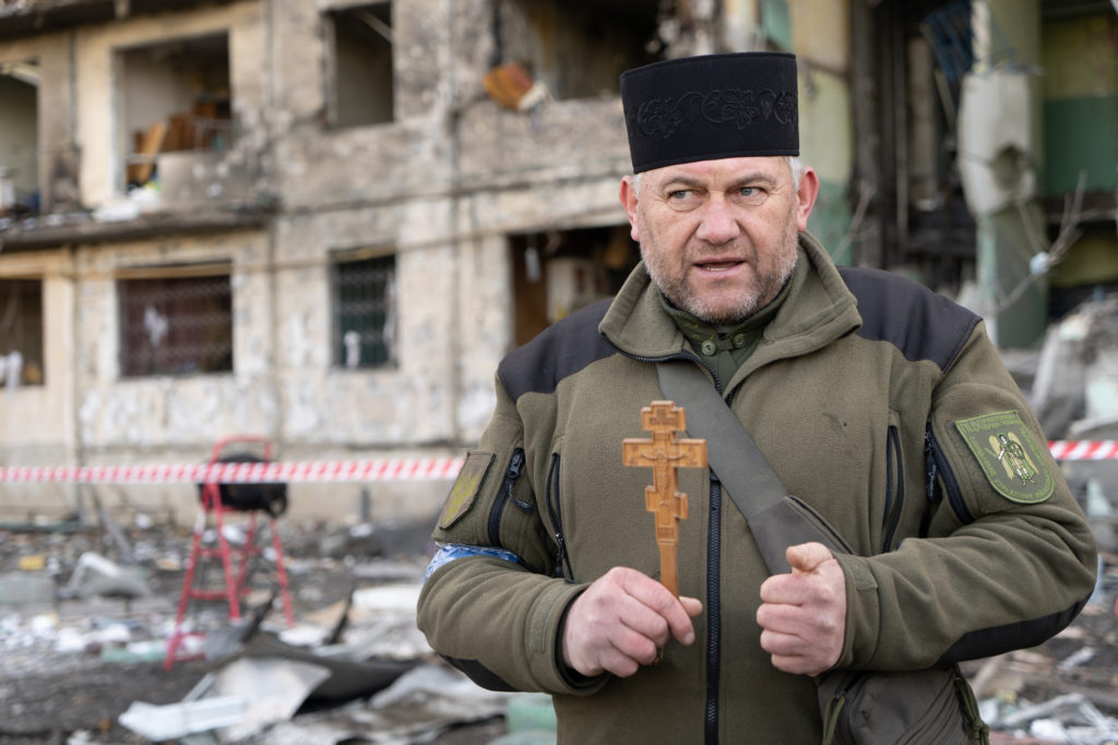 A chaplain in front of a bombed apartment building in Kyiv