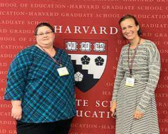 Amy Bryan posing with colleague in front of Harvard backdrop.