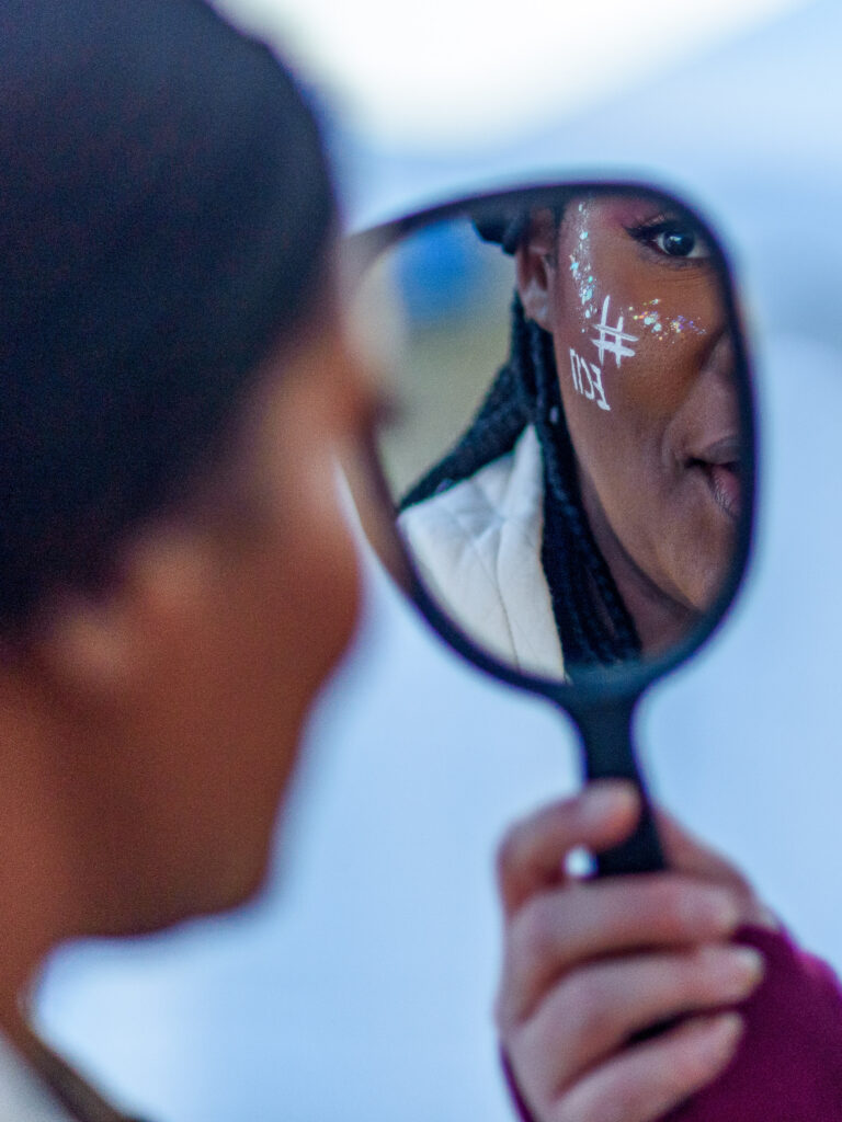 An Earlham student looks in a hand mirror at her game day makeup. 