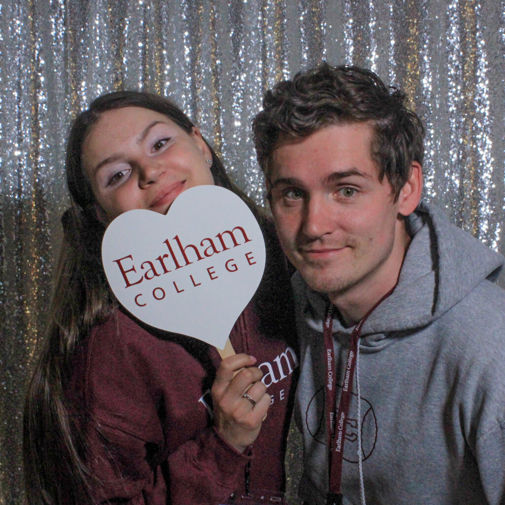 Two students posing in the photo booth with an Earlham College heart sign. 