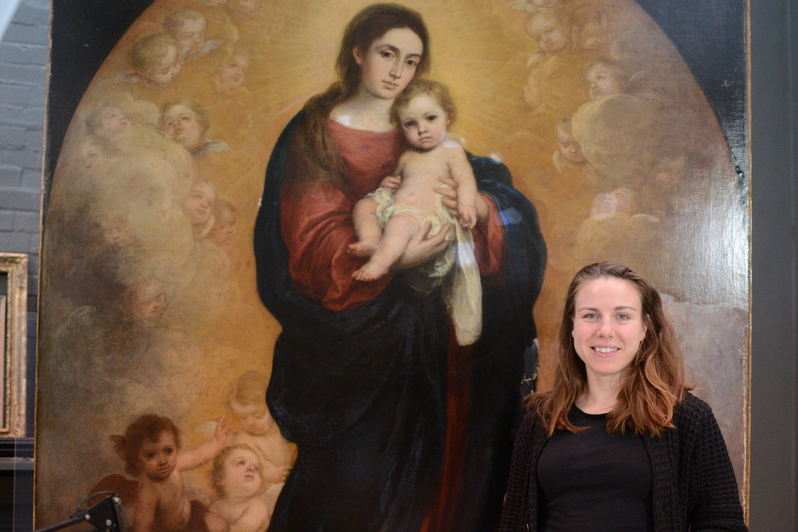 Olympia Diamond stands in front of a Murillo painting. She has long brown hair and pale skin.