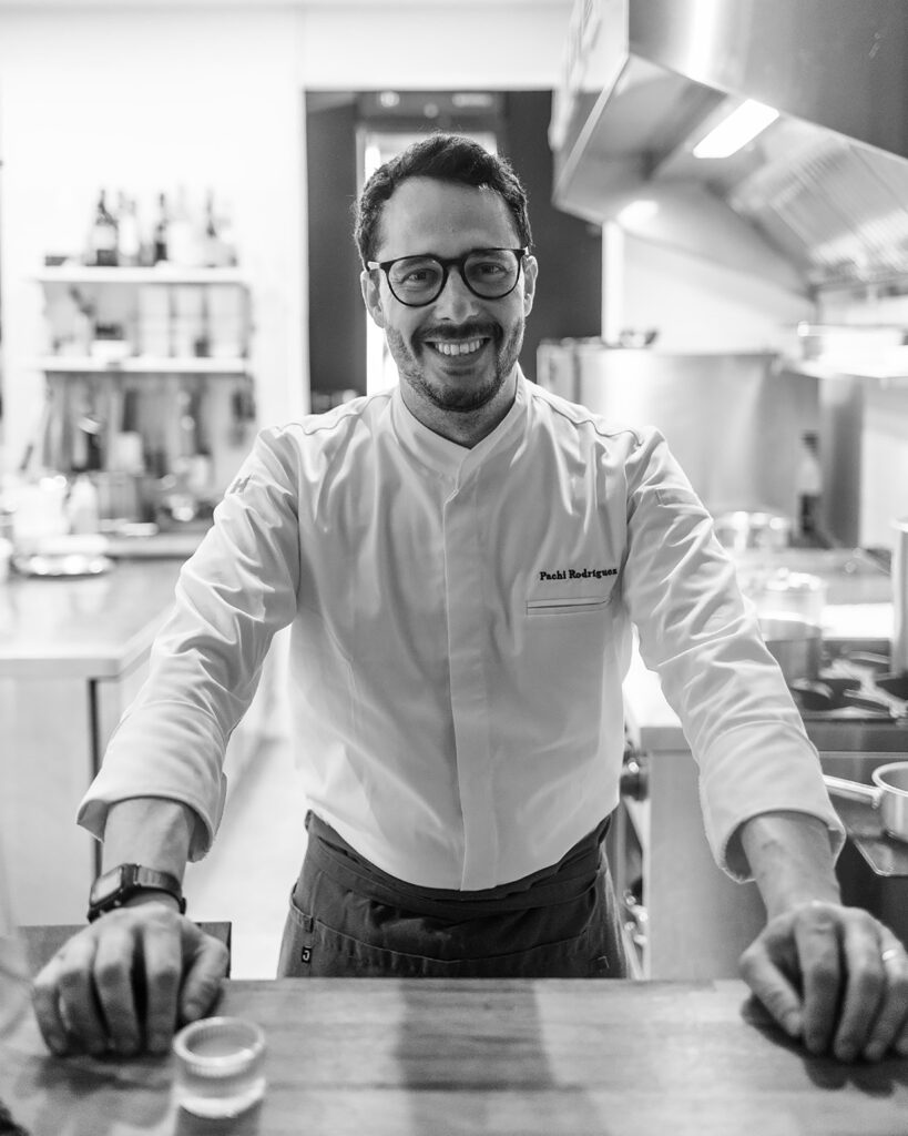 A chef stands behind his counter, smiling at the camera